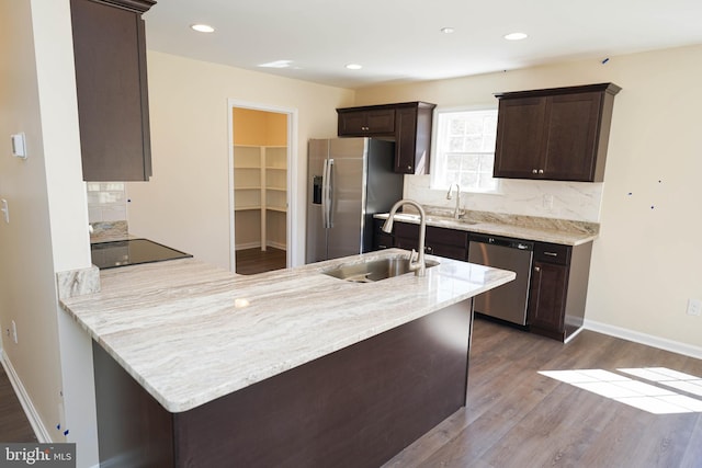 kitchen with hardwood / wood-style floors, appliances with stainless steel finishes, tasteful backsplash, sink, and kitchen peninsula