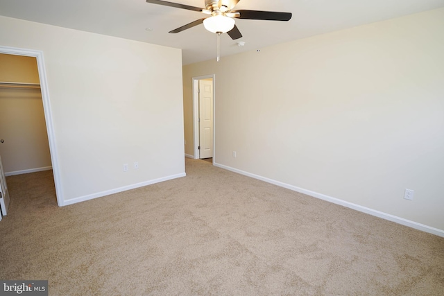 unfurnished bedroom featuring ceiling fan, a walk in closet, a closet, and light colored carpet