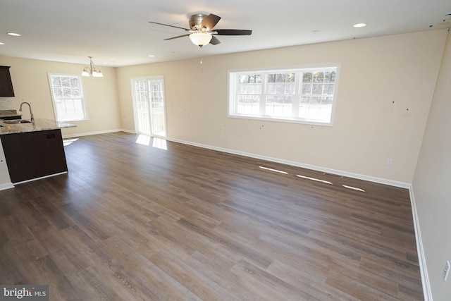 unfurnished living room featuring dark wood-type flooring, sink, and ceiling fan with notable chandelier