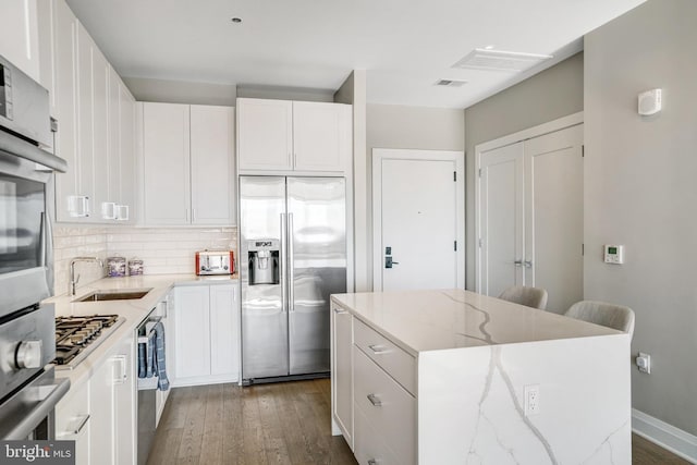 kitchen with stainless steel appliances, white cabinetry, light stone counters, and a center island