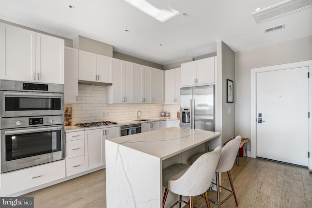 kitchen featuring white cabinetry, stainless steel appliances, a kitchen breakfast bar, light stone counters, and a center island