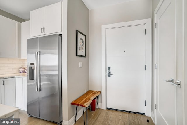 kitchen with white cabinetry, light hardwood / wood-style floors, backsplash, and stainless steel fridge