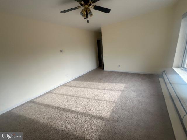 carpeted empty room with ceiling fan and a baseboard heating unit