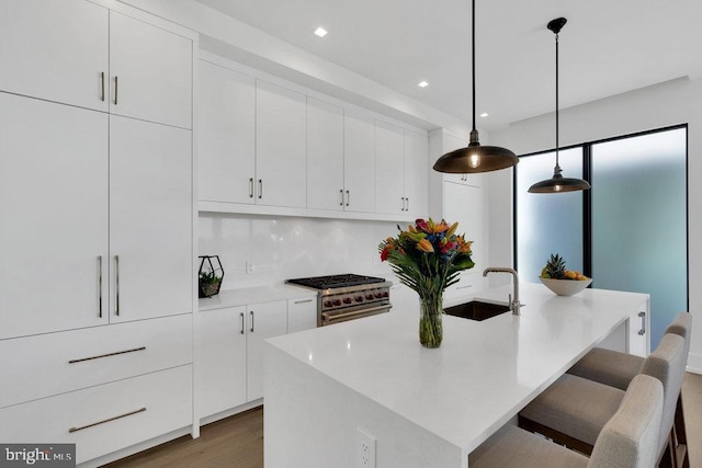 kitchen with a kitchen island with sink, hanging light fixtures, high end stainless steel range, and sink