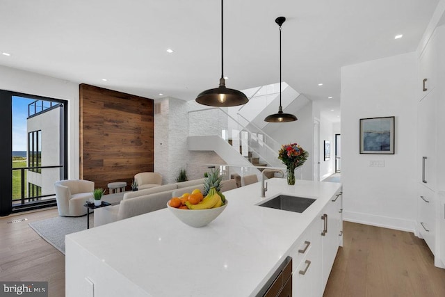 kitchen featuring sink, wood walls, a center island with sink, pendant lighting, and light hardwood / wood-style floors