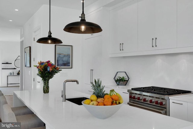 kitchen with pendant lighting, sink, high end stainless steel range oven, white cabinetry, and a kitchen bar