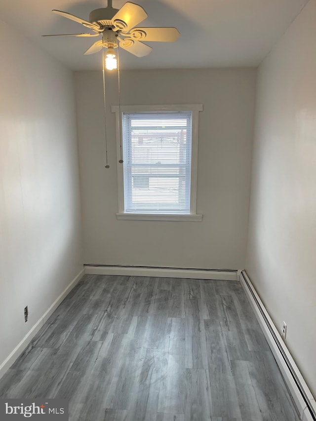 spare room with baseboards, wood finished floors, a ceiling fan, baseboard heating, and a baseboard heating unit