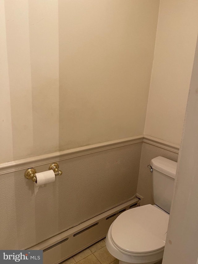 half bathroom with a wainscoted wall, toilet, and tile patterned flooring