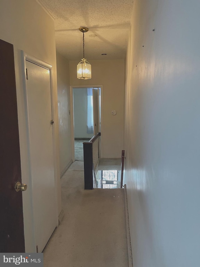 hall with an upstairs landing, a textured ceiling, a chandelier, and concrete floors