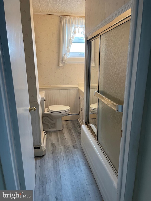 bathroom featuring a wainscoted wall, wallpapered walls, toilet, wood finished floors, and a baseboard heating unit