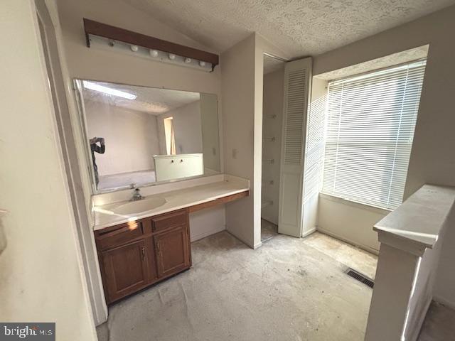 bathroom with a textured ceiling, vanity, and lofted ceiling