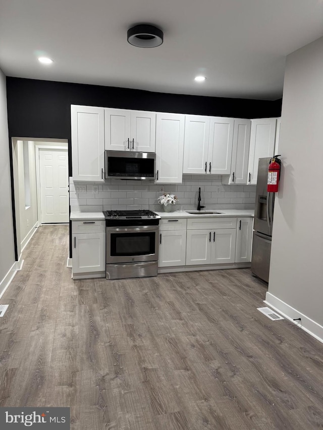 kitchen featuring white cabinets, appliances with stainless steel finishes, sink, and light wood-type flooring