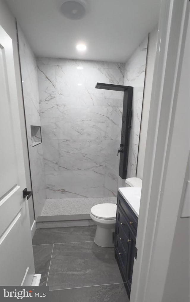 bathroom featuring a tile shower, toilet, and vanity