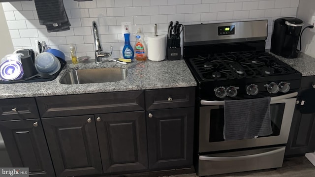 kitchen with stainless steel gas range oven, backsplash, light stone counters, and sink