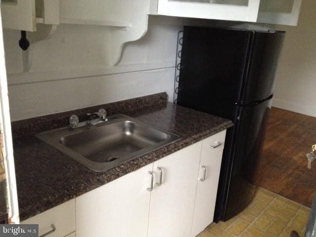 kitchen with light tile patterned floors, white cabinetry, black refrigerator, dark stone counters, and sink