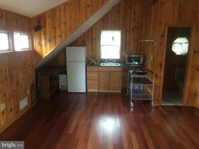 kitchen featuring white fridge, dark hardwood / wood-style floors, a healthy amount of sunlight, and wood walls