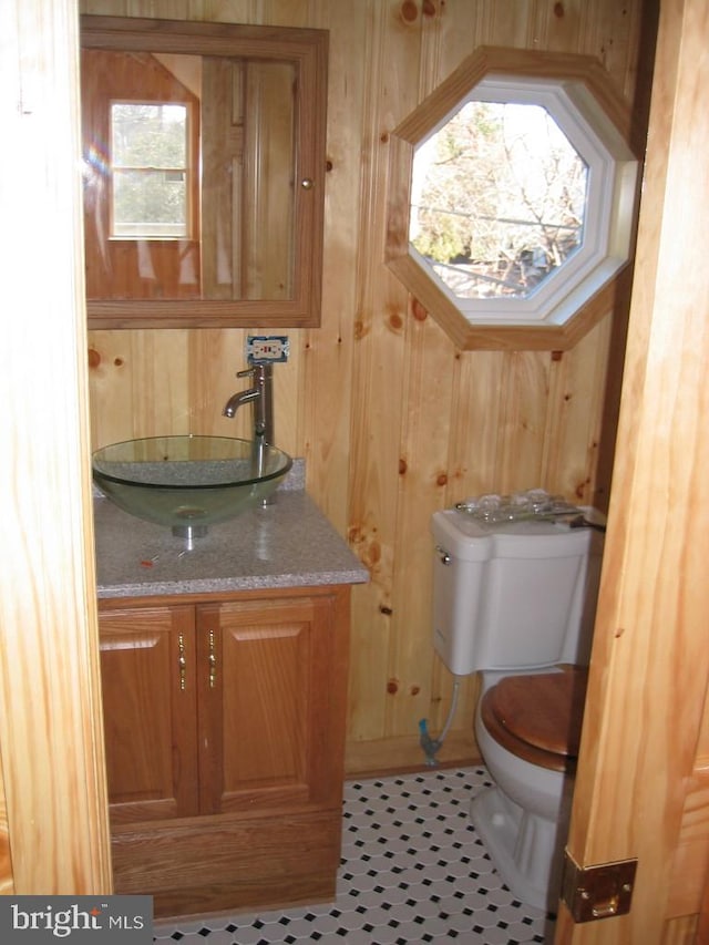 bathroom featuring toilet, tile patterned flooring, wooden walls, and vanity