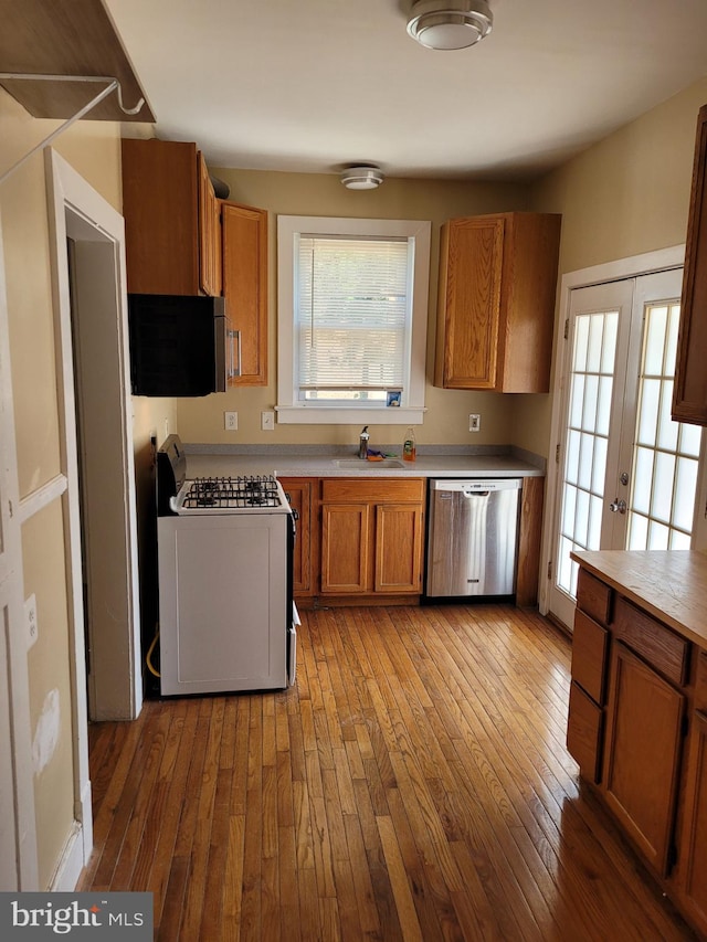 kitchen with stainless steel dishwasher, sink, light hardwood / wood-style floors, and white range with gas cooktop