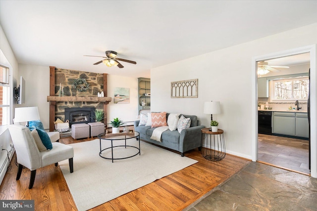 living room featuring ceiling fan, a fireplace, wood finished floors, and baseboards