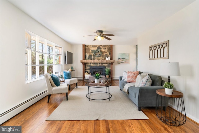 living area featuring a stone fireplace, a baseboard radiator, and wood finished floors