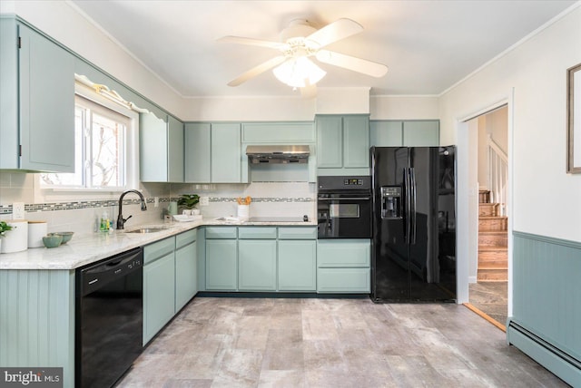 kitchen featuring a wainscoted wall, a baseboard radiator, under cabinet range hood, black appliances, and a sink