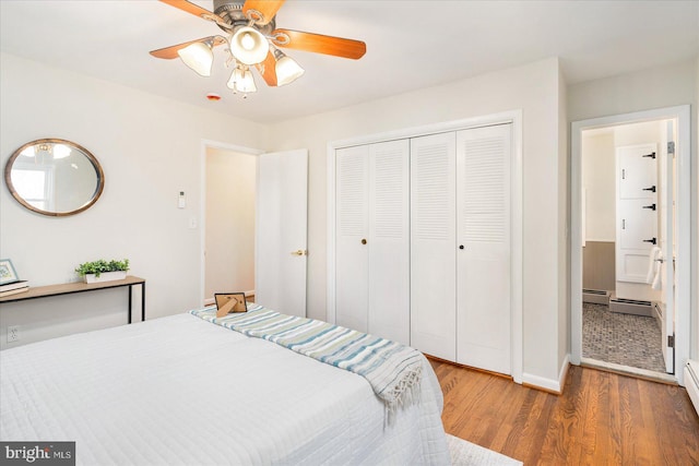 bedroom with a baseboard heating unit, ceiling fan, a closet, and wood finished floors