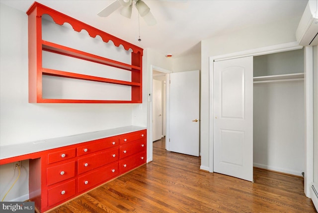 unfurnished bedroom with dark wood finished floors, a baseboard radiator, a closet, a ceiling fan, and a wall mounted air conditioner