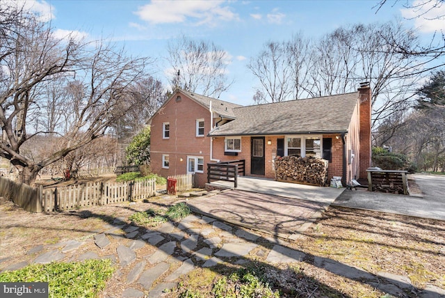 rear view of house featuring a fenced front yard, a chimney, a shingled roof, and brick siding