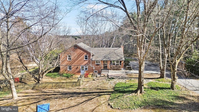 view of front of property featuring a fenced front yard, brick siding, a chimney, and dirt driveway