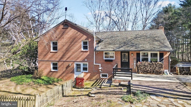 tri-level home with a shingled roof, a chimney, fence, and brick siding