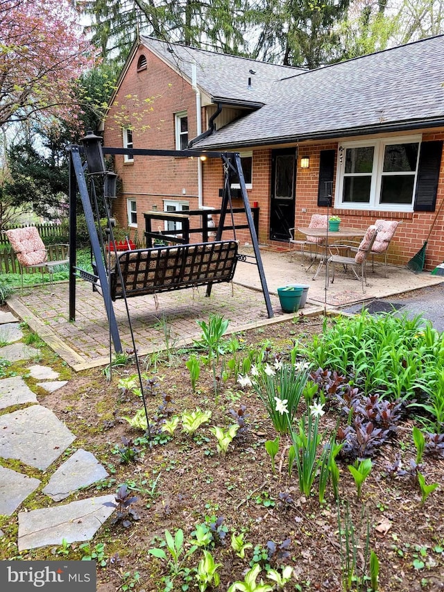 rear view of house with a patio area, a shingled roof, and brick siding