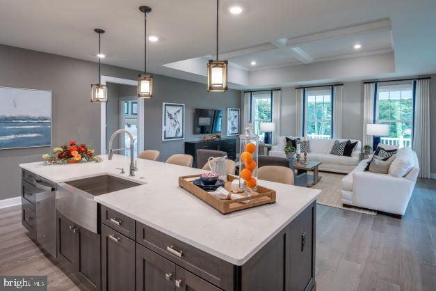 kitchen with an island with sink, decorative light fixtures, sink, coffered ceiling, and hardwood / wood-style floors