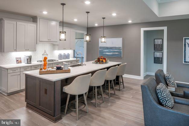 kitchen featuring an island with sink, light wood-type flooring, stainless steel gas cooktop, hanging light fixtures, and white cabinets