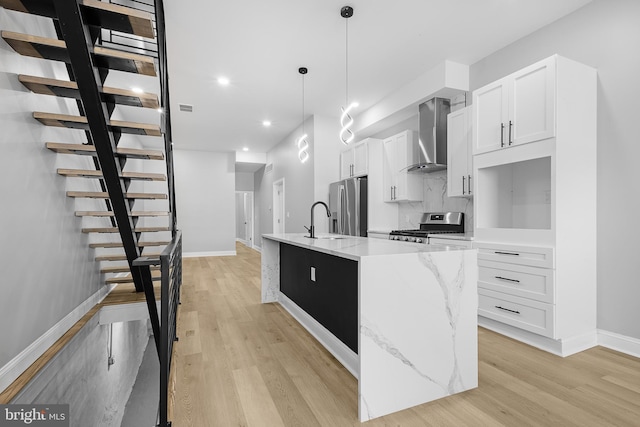 kitchen featuring light stone countertops, white cabinets, wall chimney range hood, stainless steel appliances, and a kitchen island with sink