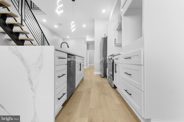 kitchen featuring stainless steel appliances, light wood-type flooring, hanging light fixtures, white cabinets, and light stone counters