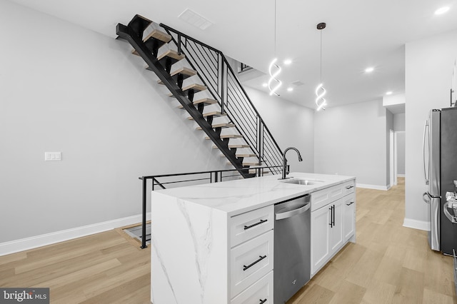 kitchen with pendant lighting, a center island with sink, sink, white cabinetry, and appliances with stainless steel finishes