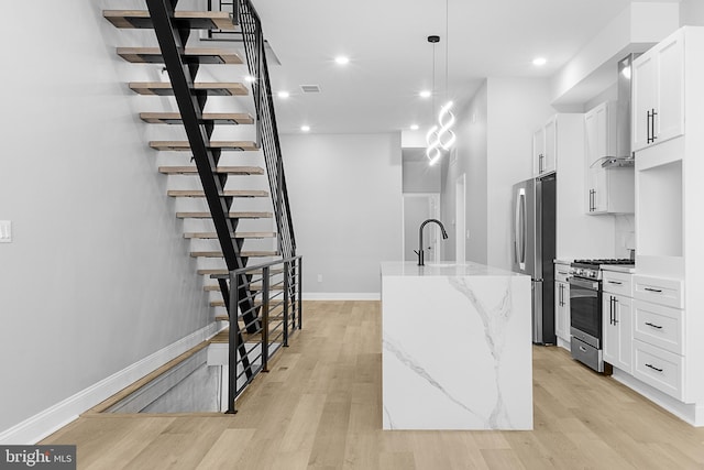 kitchen featuring sink, hanging light fixtures, appliances with stainless steel finishes, an island with sink, and white cabinets