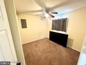 unfurnished living room featuring ceiling fan, dark colored carpet, a textured ceiling, and electric panel