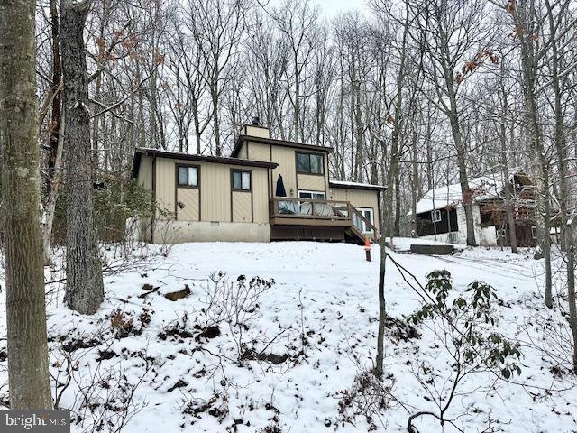 snow covered back of property with a wooden deck