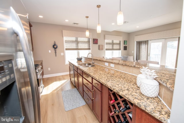 kitchen with sink, pendant lighting, stainless steel appliances, light stone countertops, and light hardwood / wood-style floors