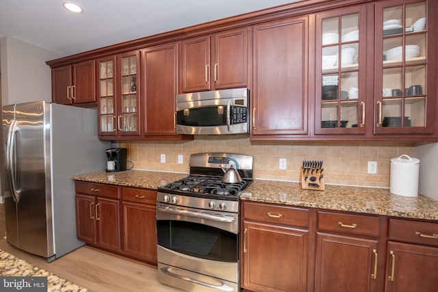 kitchen featuring appliances with stainless steel finishes, light stone countertops, light hardwood / wood-style floors, and backsplash