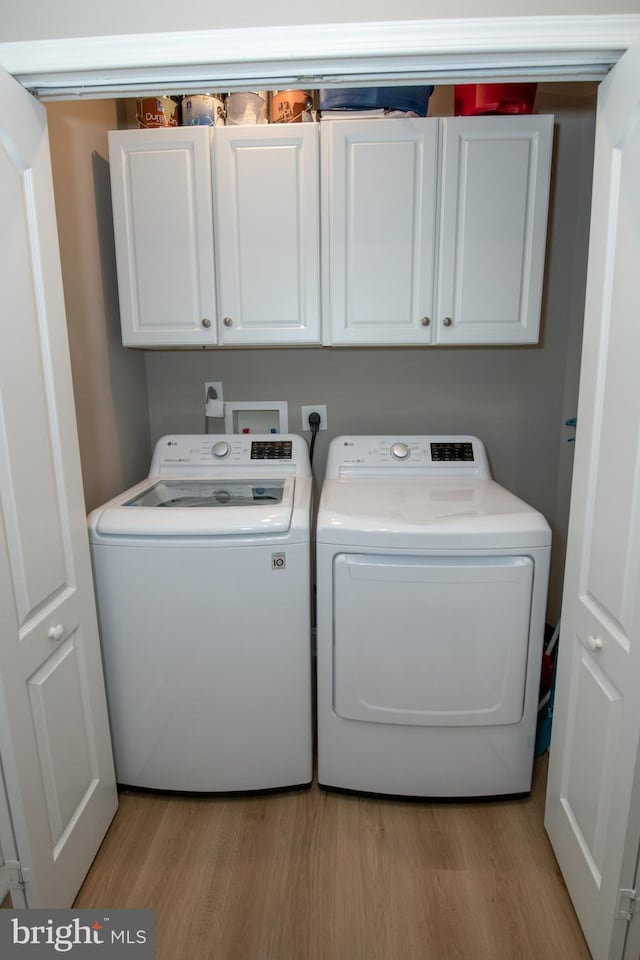 laundry room featuring independent washer and dryer, cabinets, and light hardwood / wood-style flooring