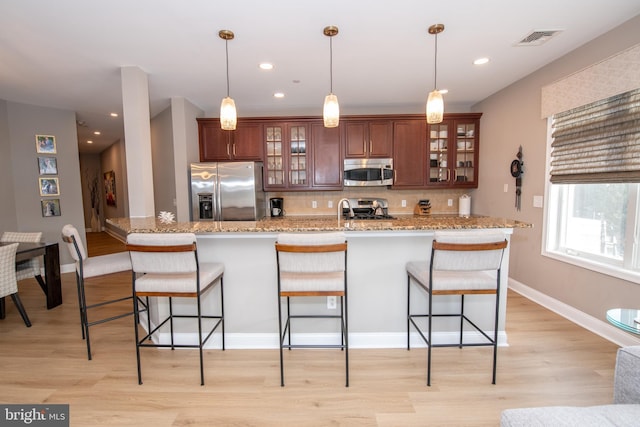 kitchen featuring a kitchen bar, tasteful backsplash, pendant lighting, stainless steel appliances, and light stone countertops