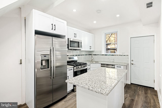 kitchen with light stone countertops, white cabinets, a kitchen island, dark hardwood / wood-style flooring, and stainless steel appliances