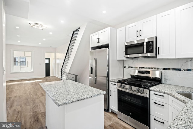 kitchen with white cabinets, light wood-type flooring, light stone countertops, and stainless steel appliances