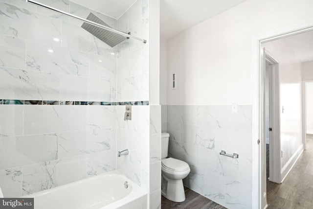 bathroom featuring hardwood / wood-style flooring, tile walls, toilet, and tiled shower / bath