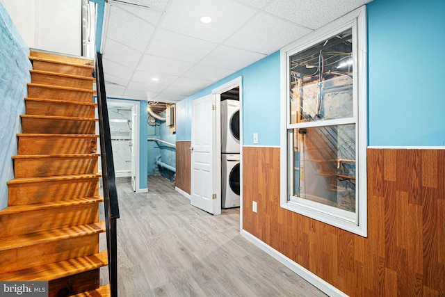 interior space featuring stacked washer / dryer, light hardwood / wood-style floors, a drop ceiling, and wooden walls