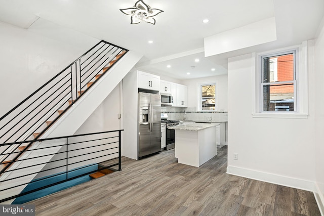 kitchen with wood-type flooring, appliances with stainless steel finishes, white cabinetry, light stone counters, and a kitchen island