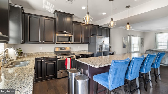 kitchen with stainless steel appliances, hanging light fixtures, a kitchen island, light stone counters, and sink