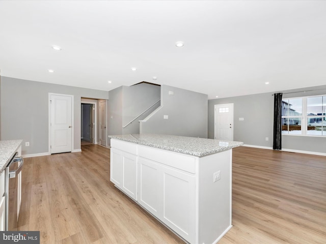 kitchen with dishwasher, a center island, light hardwood / wood-style flooring, white cabinets, and light stone counters